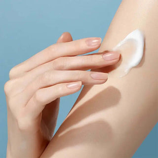 Hand applying cream to a person's arm against a blue background